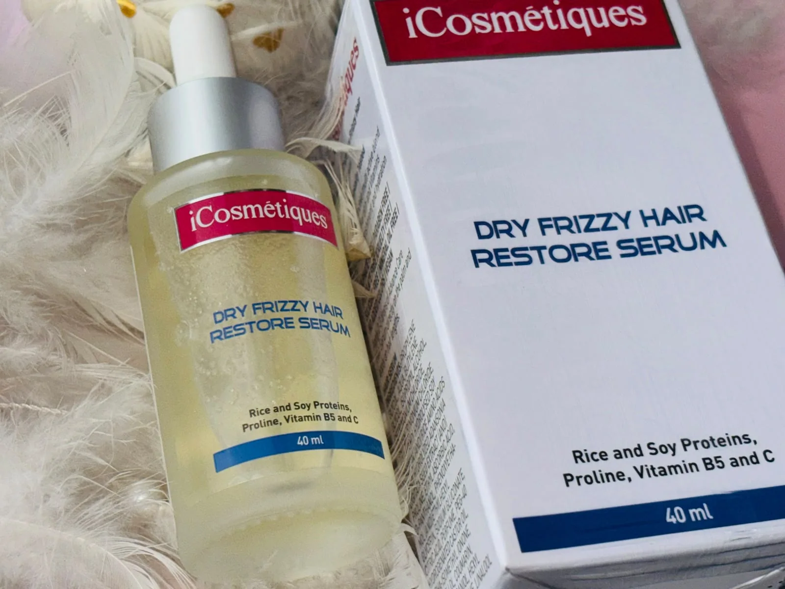 iCosmétiques Dry Frizzy Hair Restore Serum dropper bottle and box arranged on white feathers